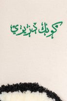 Détail de la broderie verte « Sois Algérien » en arabe sur le pull Numidie beige.