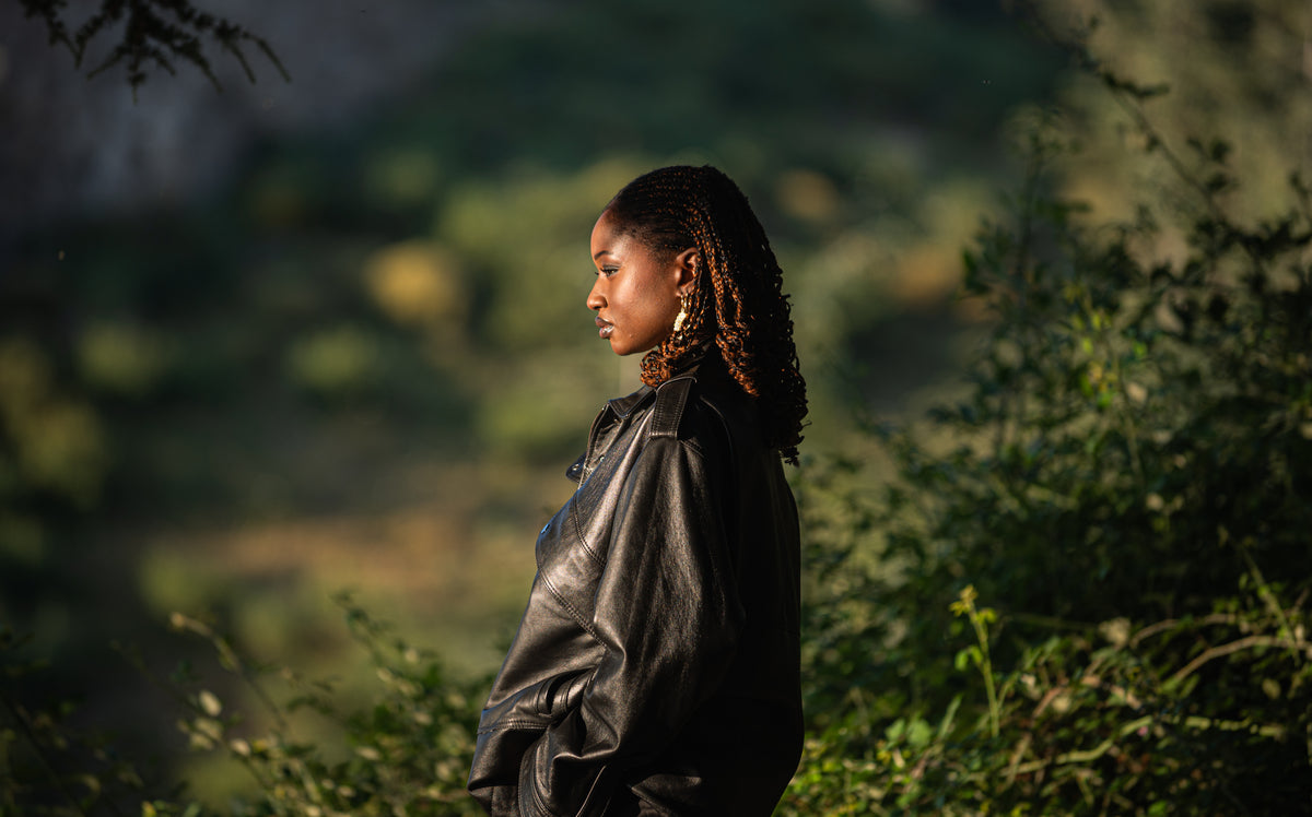 Veste Aviateur Azir en cuir noir portée par une femme, vue de profil dans un cadre naturel.
